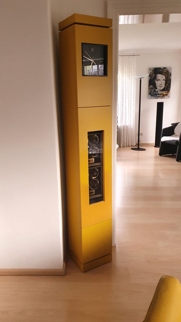 Eine gelbe Standuhr mit 8er Uhrendrehern / Uhrenbewegern im Inneren und einem schwarzem Zifferblatt
