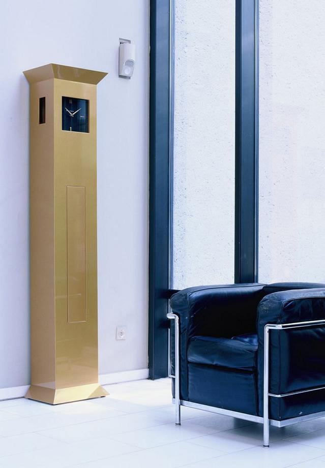 goldene Standuhr mit geschlossener Front und eleganten schwarzen Zifferblatt steht in einem Raum mit dunklen Möbeln